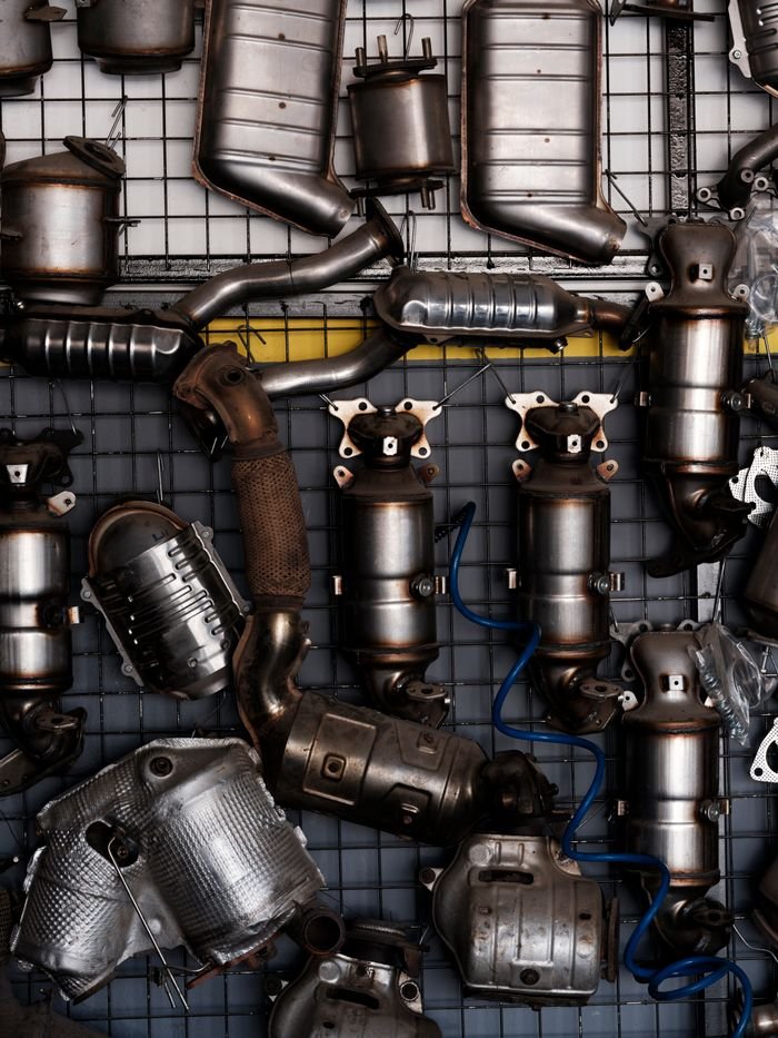 Collection of vintage car exhaust parts hanging in an industrial workshop setting.